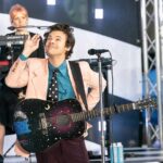 Harry Styles performing on stage with a decorated acoustic guitar