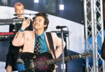 Harry Styles performing on stage with a decorated acoustic guitar
