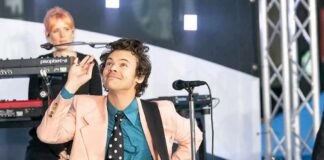 Harry Styles performing on stage with a decorated acoustic guitar