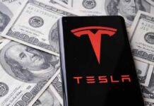 Tesla logo on smartphone over US hundred-dollar bills
