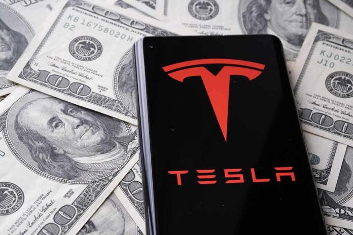 Tesla logo on smartphone over US hundred-dollar bills