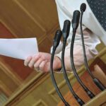 Speaker at podium holding paper near multiple microphones